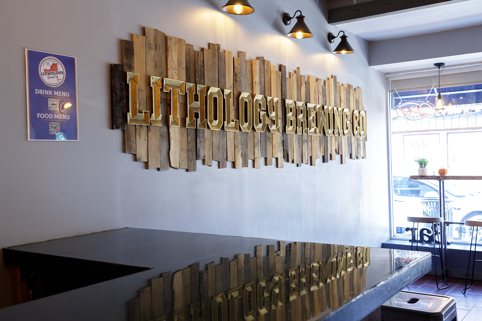Wooden sign with gold lettering on the wall next to a blue bar reading Lithology Brewing co.